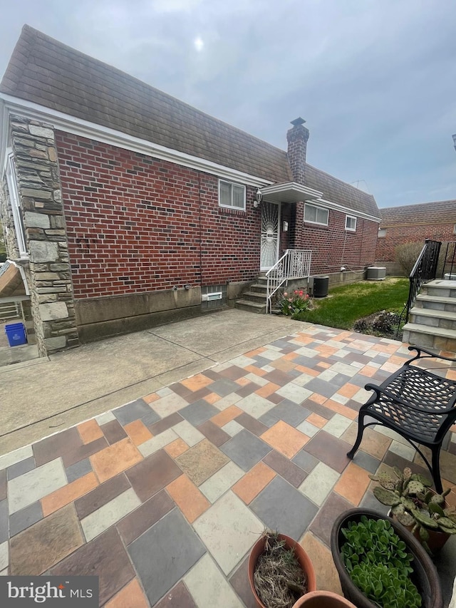 back of house with a chimney, brick siding, central air condition unit, and a patio
