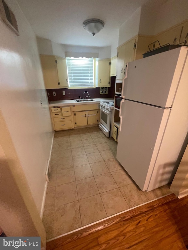 kitchen with a sink, decorative backsplash, white appliances, light tile patterned floors, and light countertops