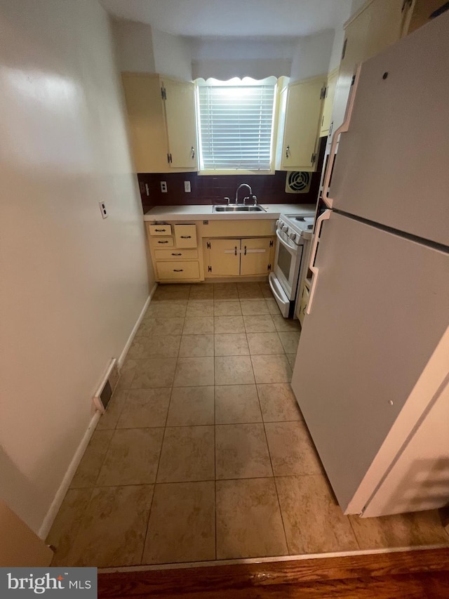 kitchen with a sink, decorative backsplash, white appliances, light tile patterned floors, and visible vents