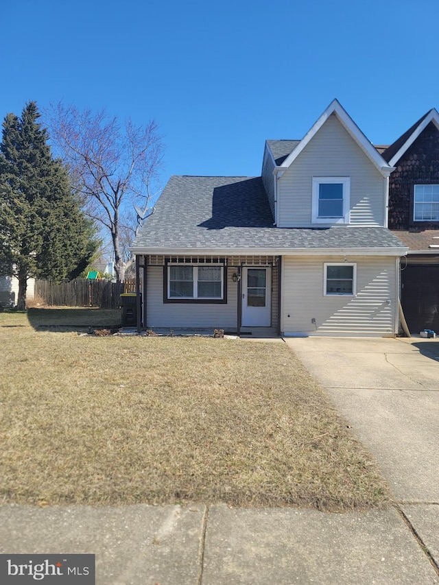 traditional-style house featuring a shingled roof, a front lawn, and fence