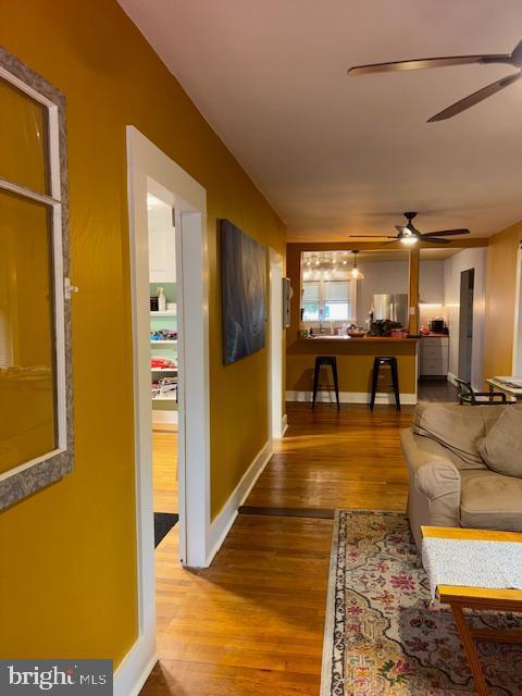 living area with baseboards, a ceiling fan, and wood finished floors