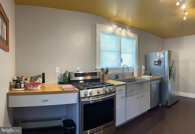 kitchen with white cabinets, butcher block countertops, appliances with stainless steel finishes, a baseboard heating unit, and a sink