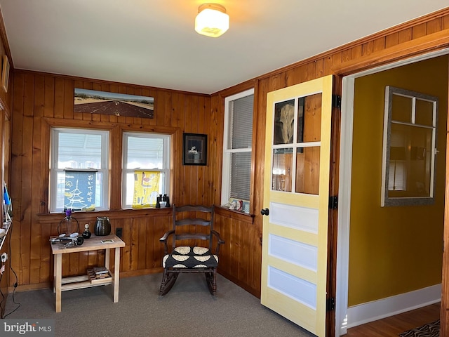 living area featuring carpet floors, wood walls, and baseboards