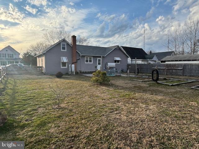 rear view of house with a yard, a chimney, and fence