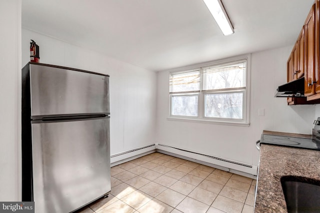 kitchen with brown cabinetry, freestanding refrigerator, a baseboard heating unit, light tile patterned flooring, and under cabinet range hood