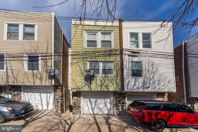 multi unit property with stone siding, an attached garage, and driveway