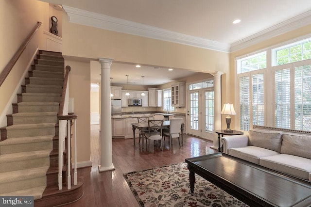 living room with decorative columns, baseboards, dark wood finished floors, ornamental molding, and stairs