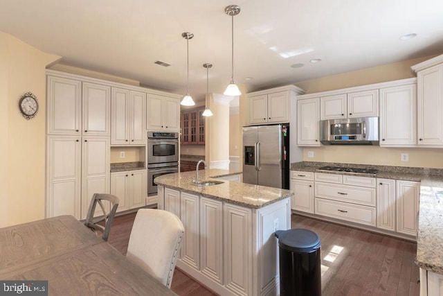 kitchen with a sink, appliances with stainless steel finishes, dark wood-style floors, an island with sink, and pendant lighting