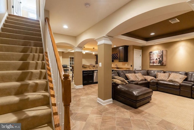 living area featuring decorative columns, visible vents, stairway, ornamental molding, and a tray ceiling