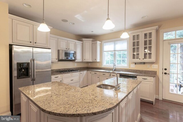 kitchen featuring a kitchen island with sink, light stone counters, stainless steel appliances, and a sink