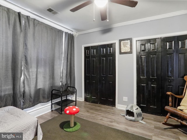 interior space with wood finished floors, a ceiling fan, baseboards, visible vents, and crown molding