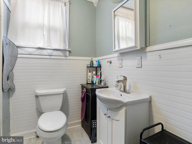 half bath featuring a wainscoted wall, vanity, and toilet