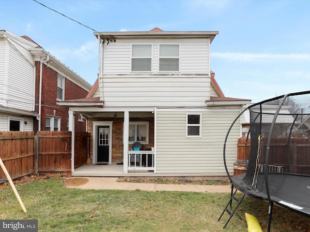 back of house with a trampoline, fence private yard, a lawn, and a patio