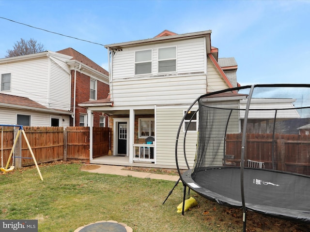 back of house with a patio, a trampoline, a fenced backyard, and a lawn