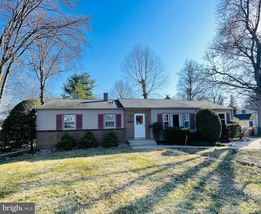 view of front of house featuring brick siding, a chimney, and a front yard