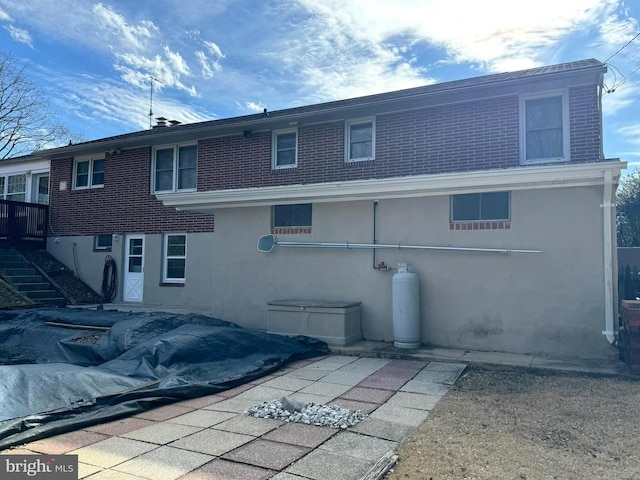 back of house with stairs, brick siding, and stucco siding