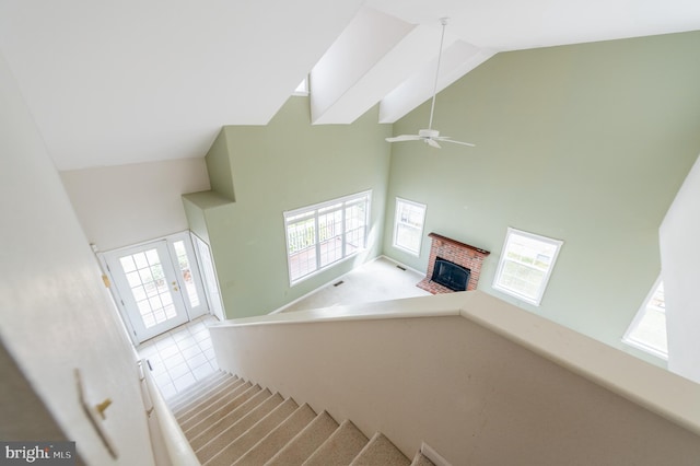 stairs with high vaulted ceiling, french doors, a fireplace, and a ceiling fan