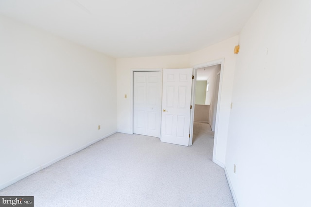 unfurnished bedroom featuring light carpet, baseboards, and a closet