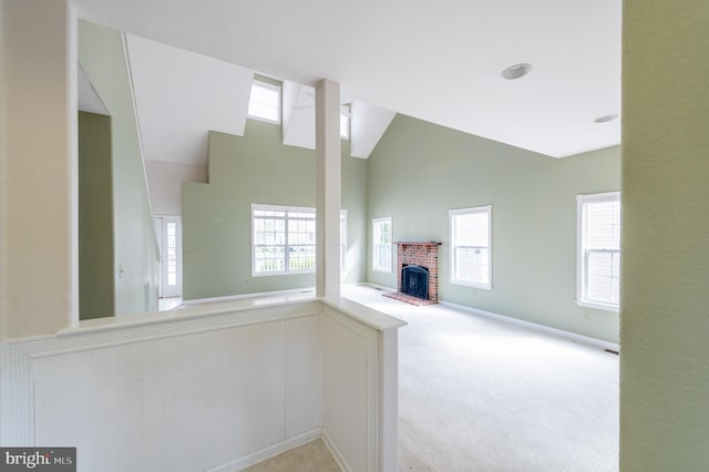 unfurnished living room with high vaulted ceiling, a brick fireplace, a healthy amount of sunlight, and light carpet