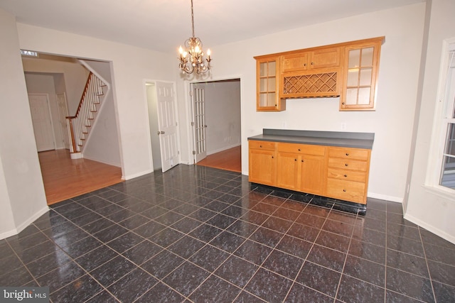 kitchen featuring baseboards, dark countertops, glass insert cabinets, decorative light fixtures, and an inviting chandelier