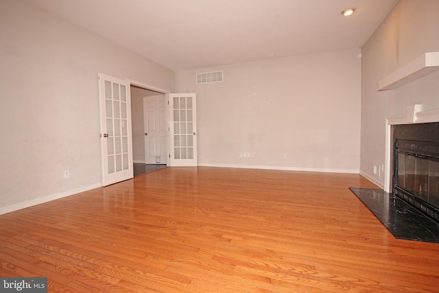 unfurnished living room featuring wood finished floors, visible vents, a high end fireplace, baseboards, and french doors