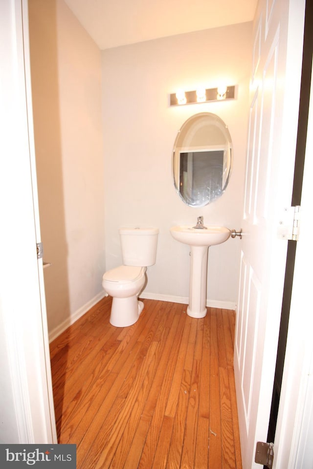 half bath featuring baseboards, toilet, and wood finished floors