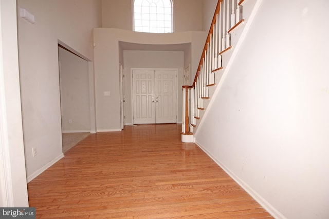 hall featuring a high ceiling, stairway, light wood-style flooring, and baseboards