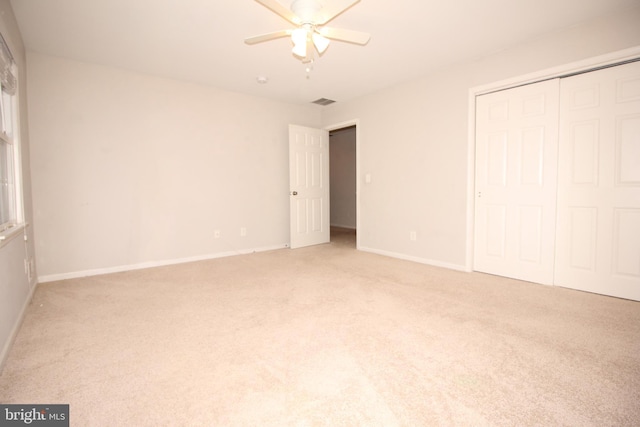 unfurnished bedroom with a closet, light carpet, ceiling fan, and baseboards