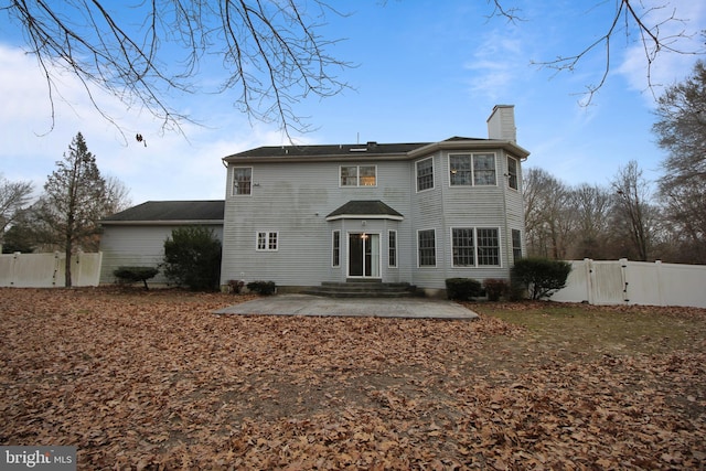 back of house with a chimney, a patio area, fence, and a gate