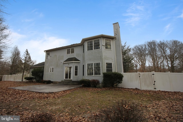 rear view of house with entry steps, a patio, fence, a gate, and a chimney