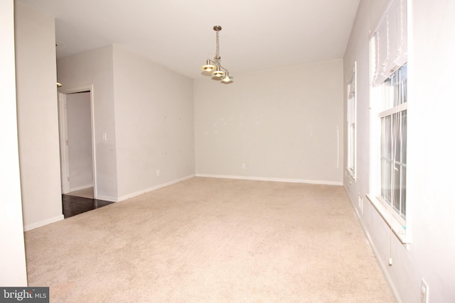 carpeted spare room featuring baseboards and a notable chandelier