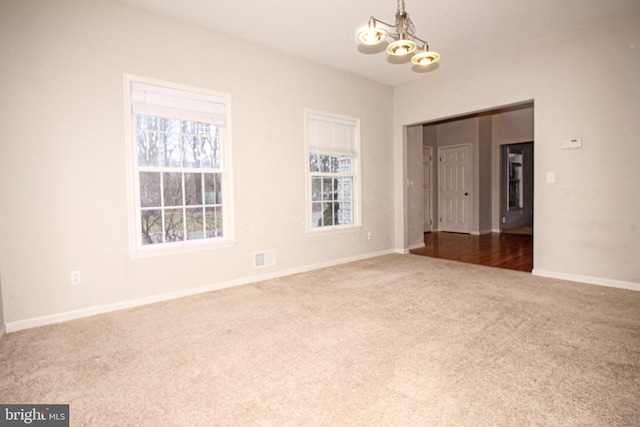 empty room featuring carpet flooring, a notable chandelier, visible vents, and baseboards