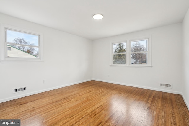 empty room featuring wood finished floors, visible vents, and baseboards