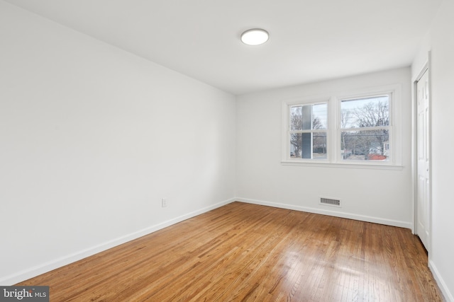 empty room featuring light wood-type flooring, visible vents, and baseboards