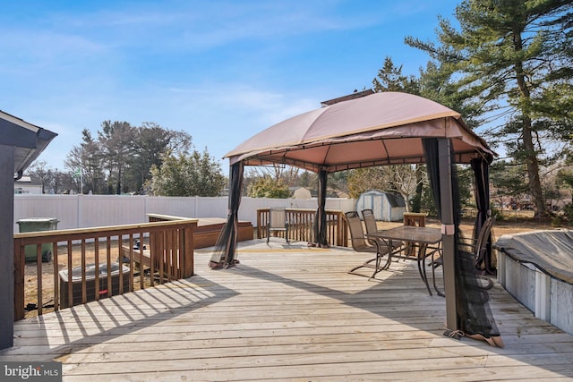 wooden terrace featuring a gazebo, an outbuilding, a fenced backyard, and a storage shed