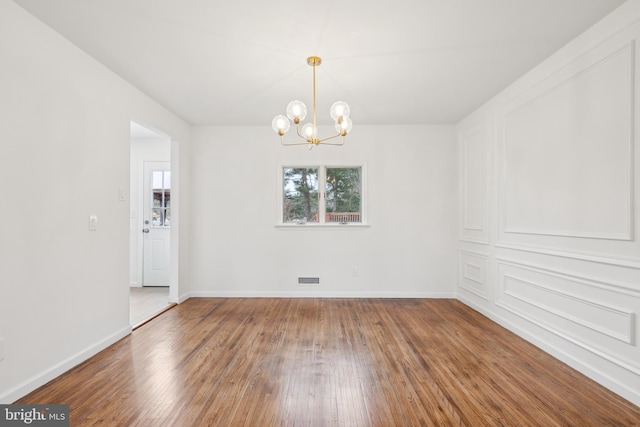 spare room featuring an inviting chandelier, visible vents, baseboards, and wood finished floors