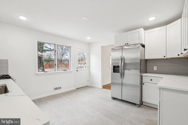 kitchen with tasteful backsplash, white cabinets, visible vents, and stainless steel fridge with ice dispenser