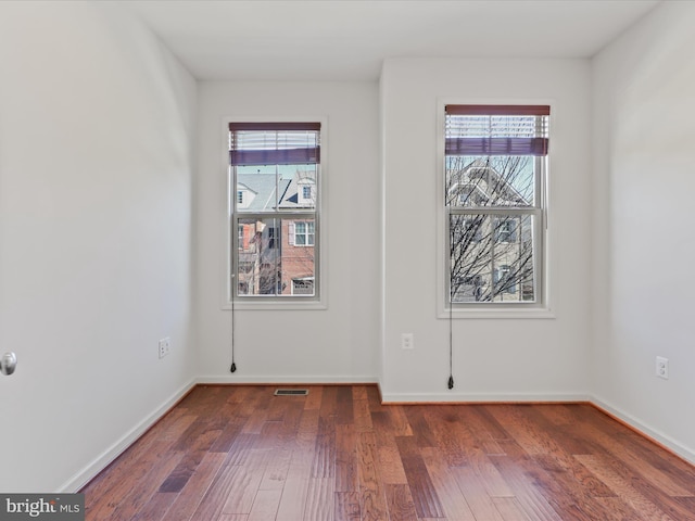 spare room with visible vents, wood finished floors, a wealth of natural light, and baseboards