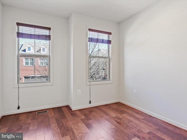 unfurnished room featuring dark wood-style floors, visible vents, and baseboards