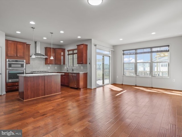 kitchen with dark wood finished floors, decorative backsplash, wall chimney exhaust hood, appliances with stainless steel finishes, and a sink