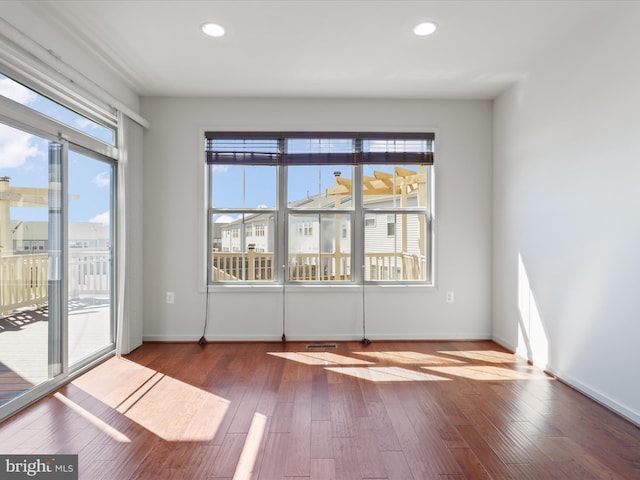 spare room featuring baseboards, recessed lighting, wood finished floors, and a healthy amount of sunlight