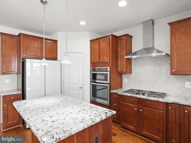 kitchen featuring stainless steel appliances, wall chimney range hood, decorative backsplash, and light stone countertops