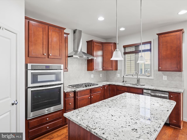 kitchen with wall chimney exhaust hood, dark wood-type flooring, light stone countertops, stainless steel appliances, and a sink