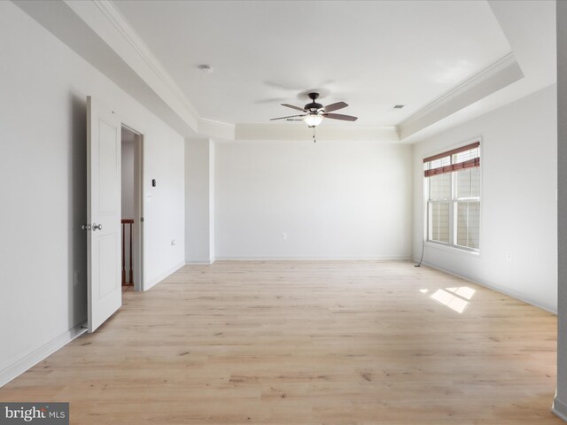 spare room featuring a tray ceiling, light wood-type flooring, visible vents, and crown molding