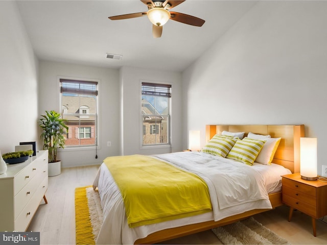 bedroom featuring light wood-style floors, ceiling fan, visible vents, and vaulted ceiling