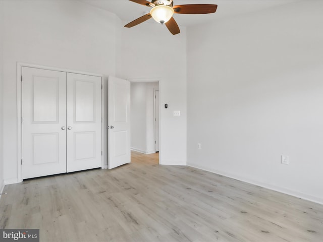 unfurnished bedroom with wood finished floors, a towering ceiling, baseboards, a ceiling fan, and a closet