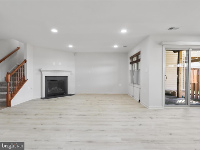 unfurnished living room featuring a fireplace with flush hearth, light wood-type flooring, stairway, and recessed lighting