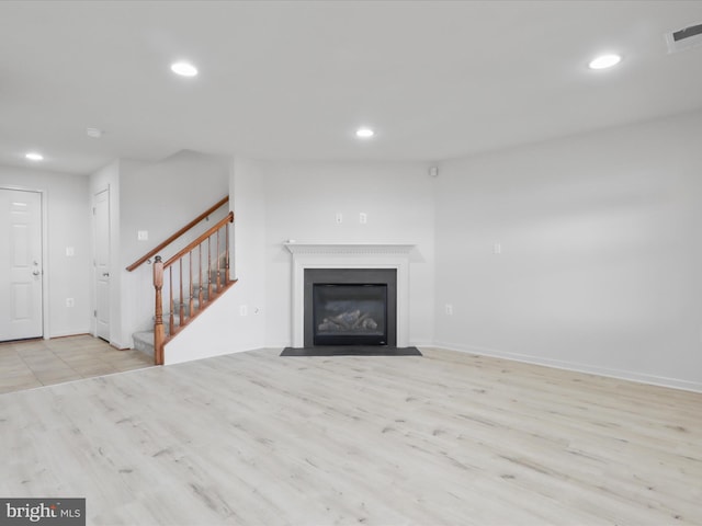 unfurnished living room with light wood finished floors, visible vents, stairway, and recessed lighting