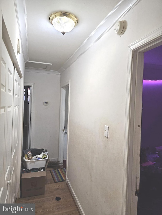 hallway featuring attic access, wood finished floors, baseboards, and ornamental molding