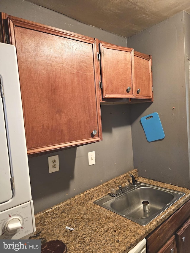 kitchen featuring dark countertops, stacked washing maching and dryer, brown cabinets, and a sink